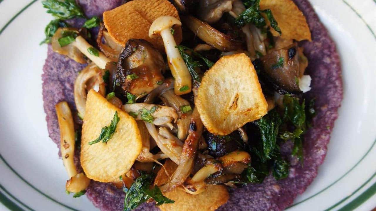 Blue corn hard taco shell with mushrooms and broccolini on a plate.