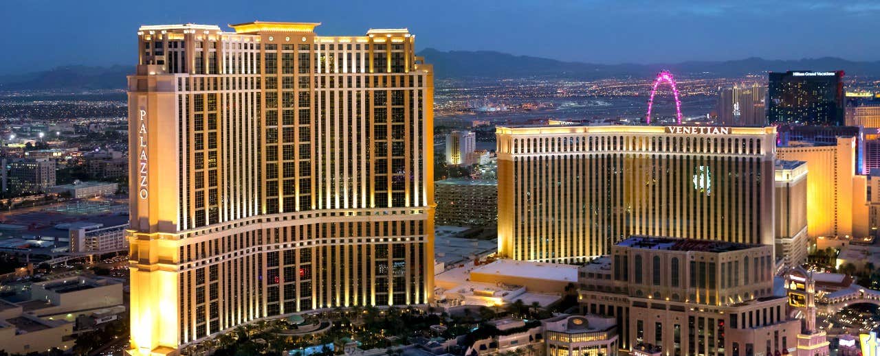 Aerial view of the Palazzo and the Venetian hotels in Las Vegas lit up at dusk, with the cityscape in the background.