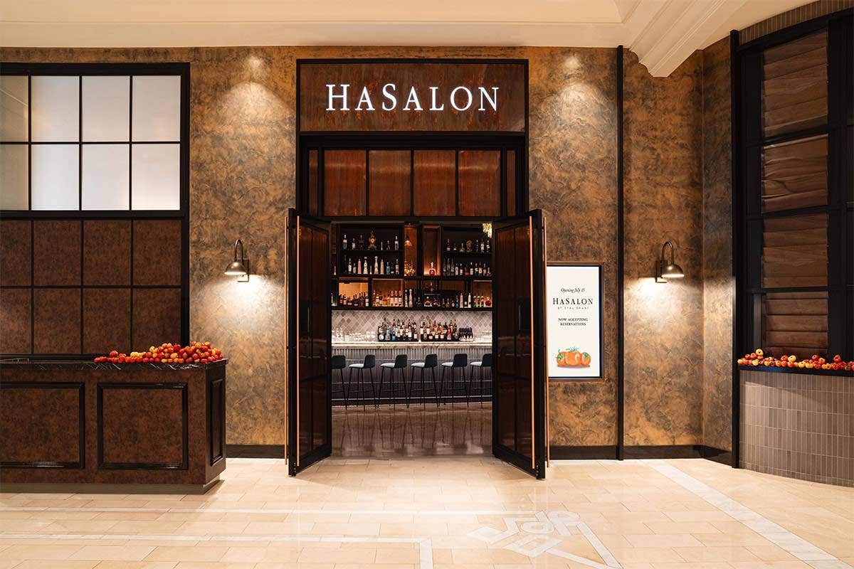Entrance to Hasalon restaurant with open doors, displaying a bar and stools inside, elegant lighting, and decorative walls.