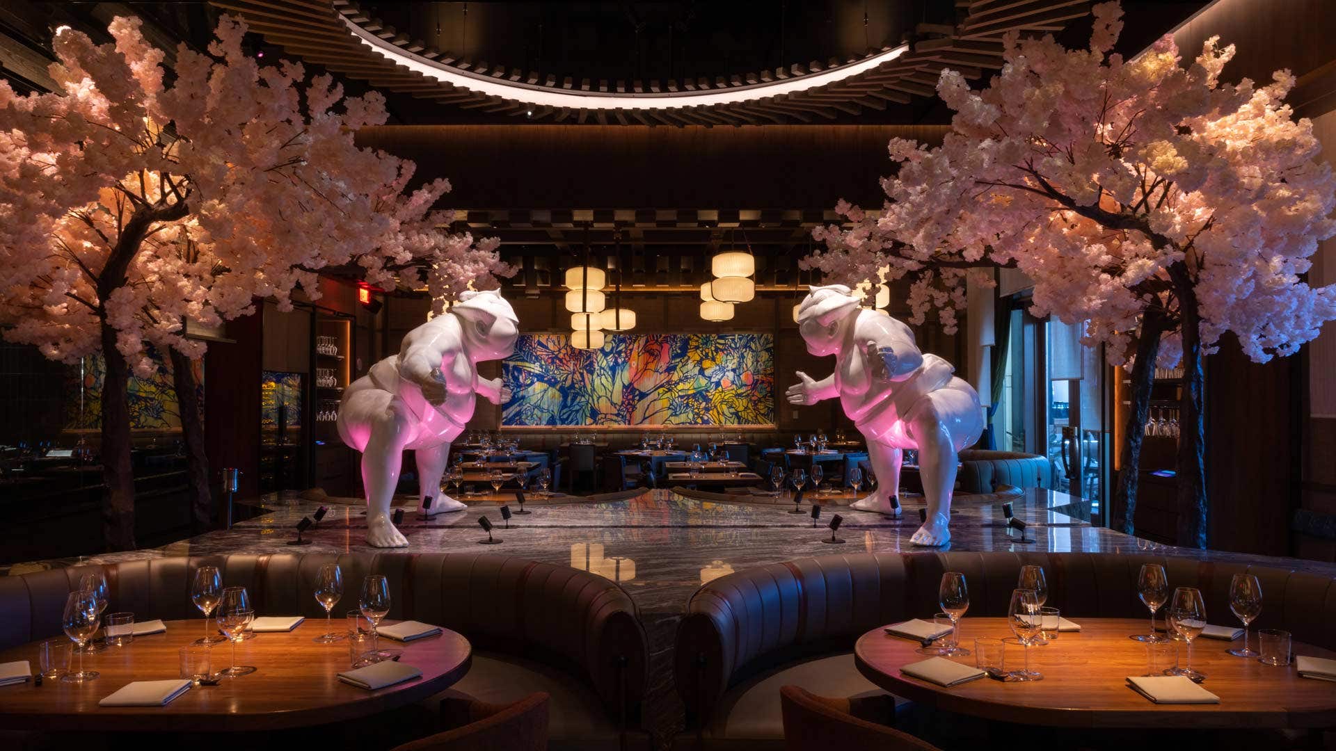 A stylish Japanese restaurant with two white sculptures and cherry blossom trees, soft pink lighting, and elegant table settings.