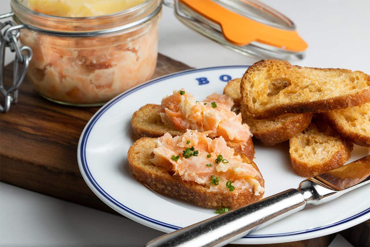 Toasted bread with salmon spread on a plate, served with a jar of salmon spread and a knife on the side.