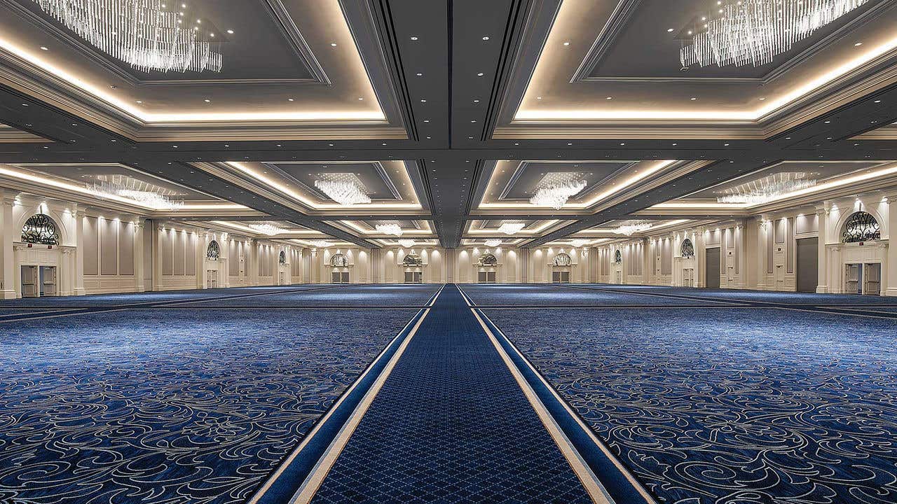 Large empty ballroom with white walls, blue carpet and chandeliers hanging from the ceiling.