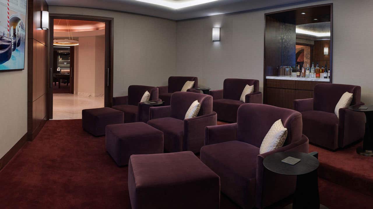 A home theater room with six large lounge chairs on a bi-level, a bar, and a TV on the wall.