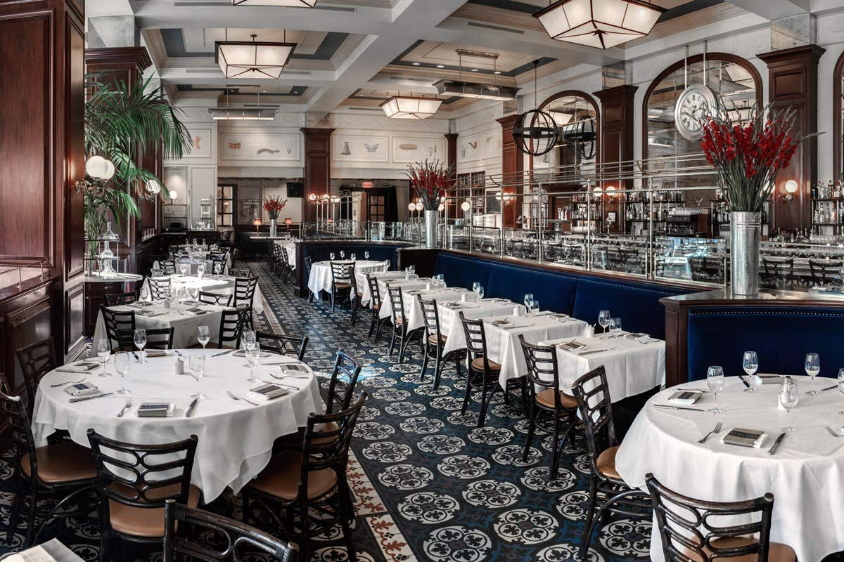 Elegant restaurant with round tables covered in white cloths, dark wooden chairs, and ornate floor tiles.