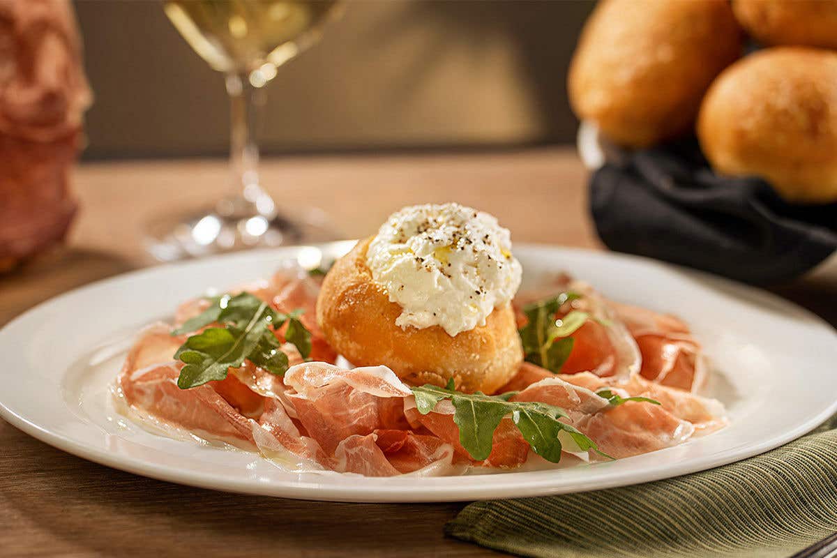 Pizza crust topped with prosciutto and a ball of stracchino cheese in the middle. 