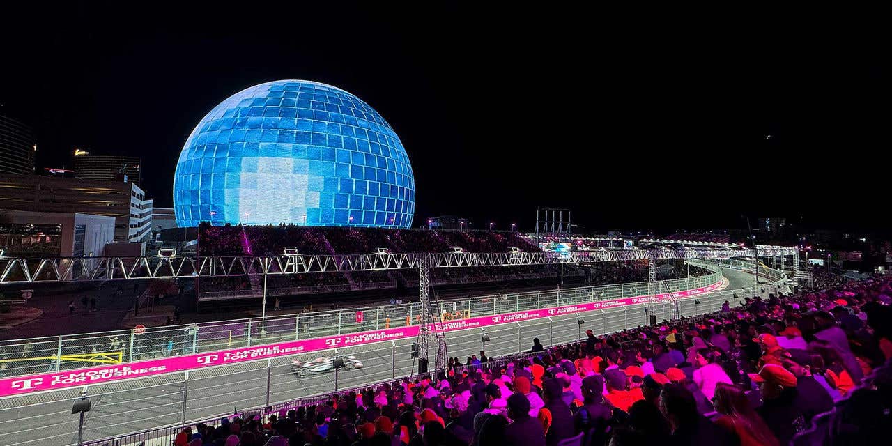 A view of a illuminated race track at night leading from the bottom left and curving upwards at the right, circling around the Sphere at The Venetian showing a blue disco ball pattern