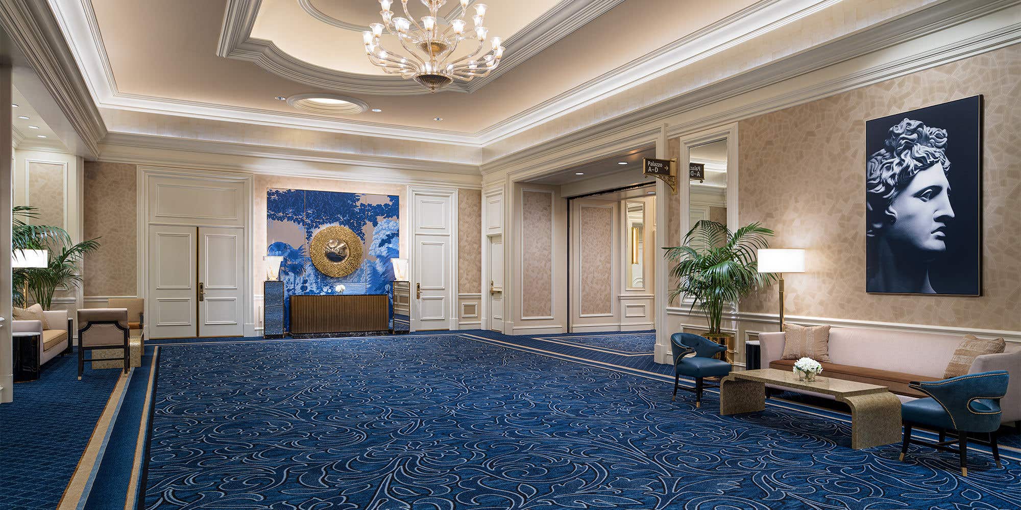 Luxurious hotel lobby with blue patterned carpet, elegant seating area, chandelier, and decorative artwork.