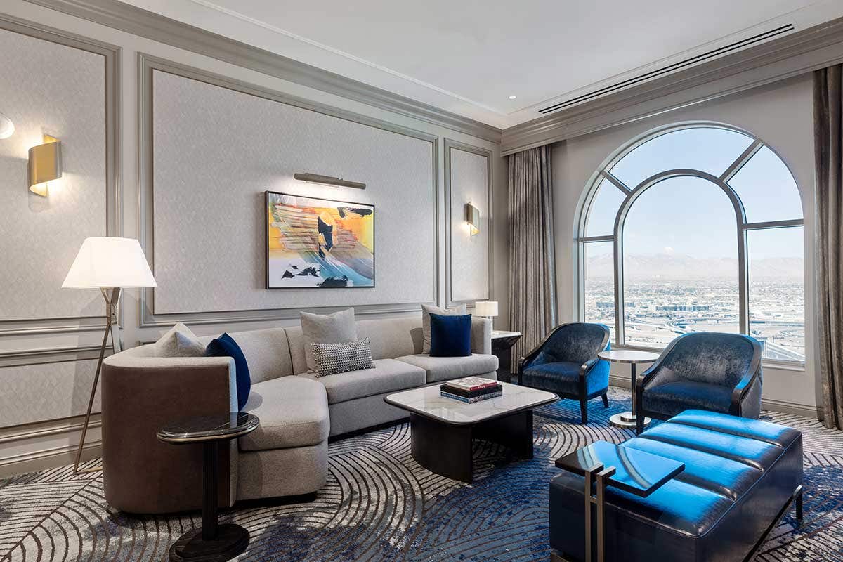 Elegant living room with a gray sofa, large arch window, blue velvet chairs, and abstract wall art.