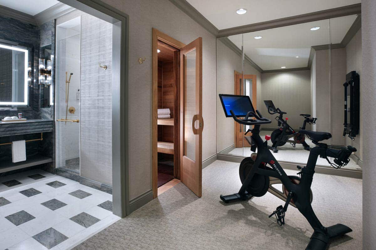 A workout room attached to a bathroom with a Peloton Bike, Tonal machine on the wall, mirrored wall, and cedar-wood dry sauna.