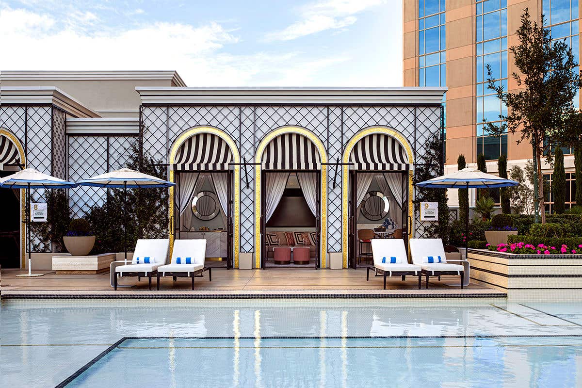Poolside cabanas with striped awnings and four lounge chairs in front, towels neatly placed on each chair.