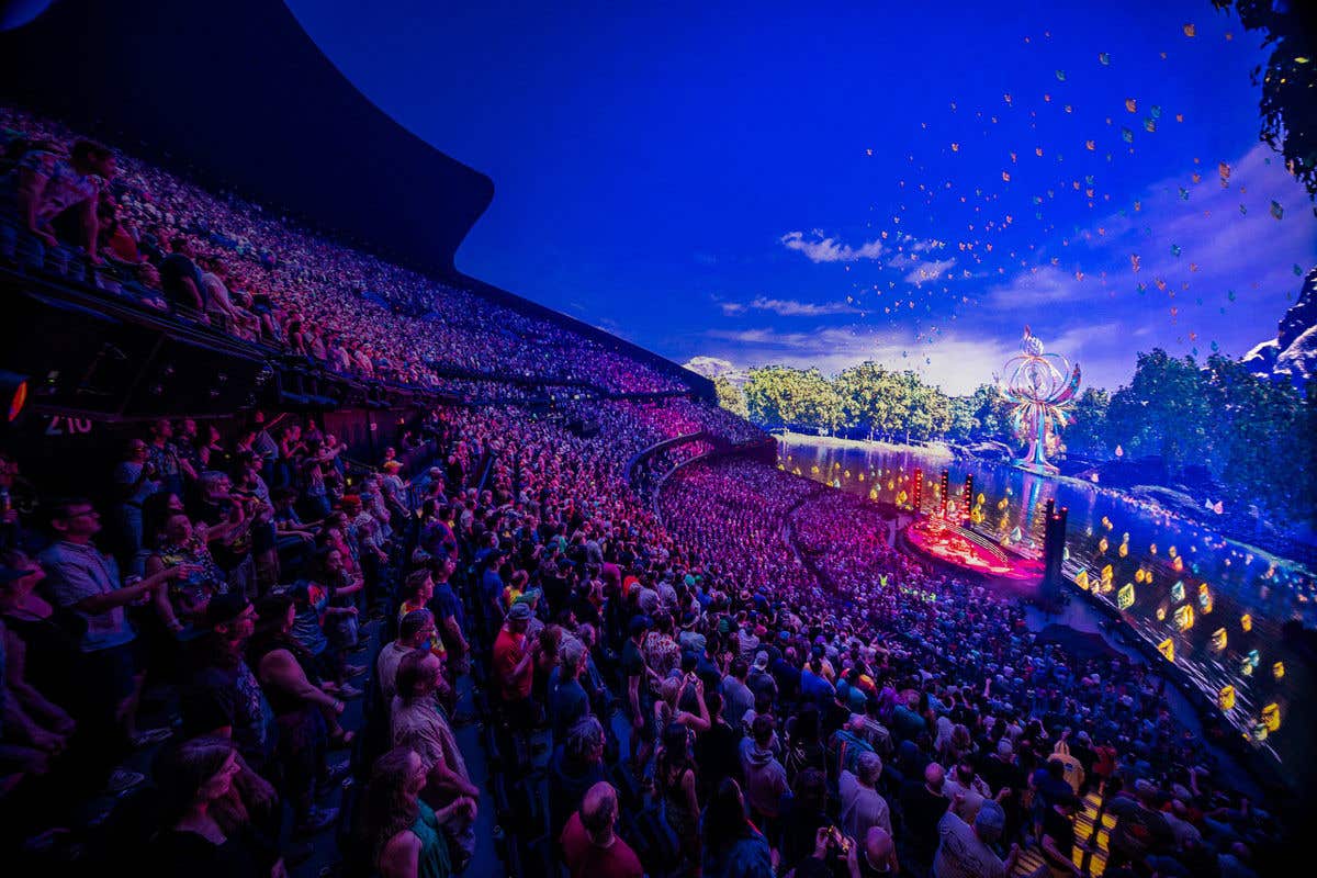 Inside Sphere packed with audience with colorful lights and a nature-themed stage.