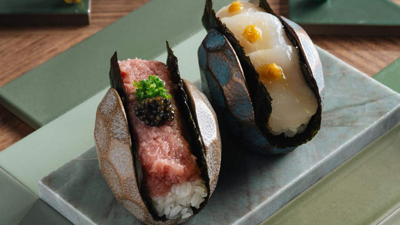 Two sushi pieces on a stone platter, featuring pink fish with caviar and white fish with orange garnish, in ceramic holders.