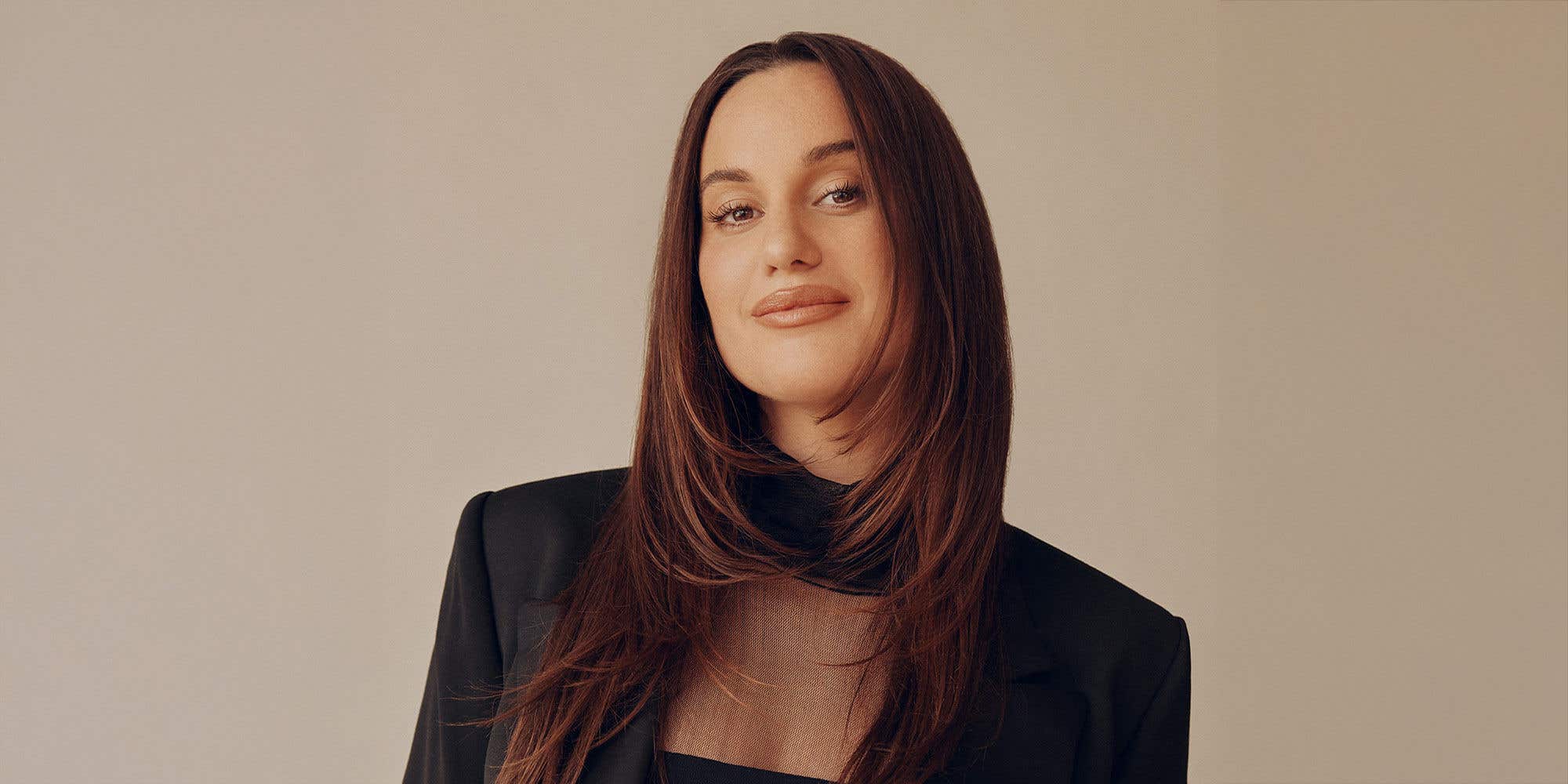 Comedian Hannah Berner, wearing a black blazer set against a gold background.