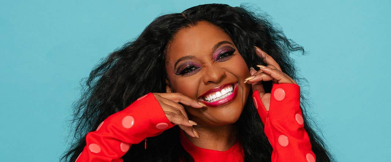Sherri Shepherd in red and pink polka dotted top in front of blue background. 