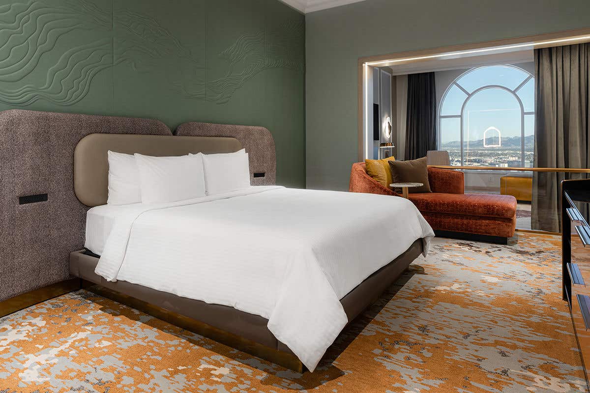 The bedroom of the Grand One Bedroom Suite with a king-sized bed, seating area, and a scenic window view. 