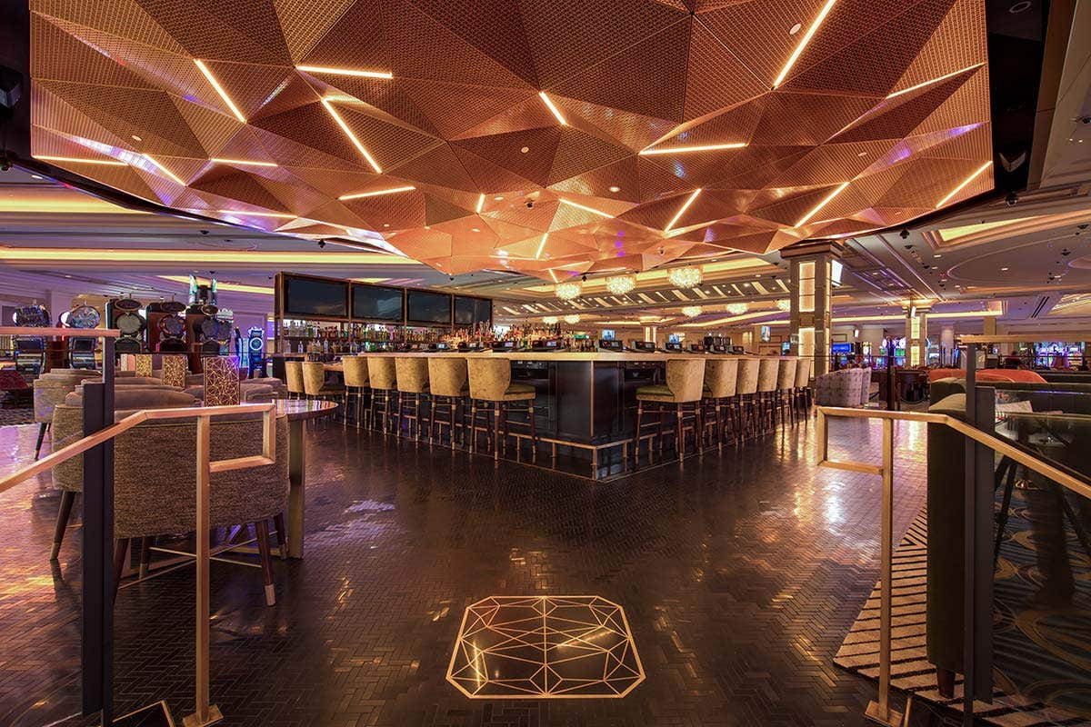 Modern, stylish bar with geometric ceiling lights, surrounded by high chairs and a shiny, reflective floor.