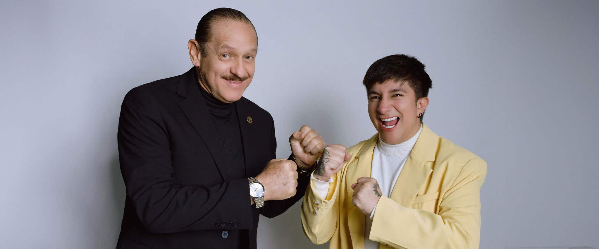 Teo González & Mario Aguilar smiling, posing with fists up; one in a black suit, the other in a yellow blazer.
