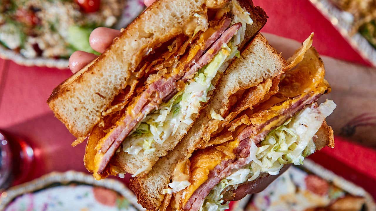 Large sandwich with col slaw, bologna, and cheese being held