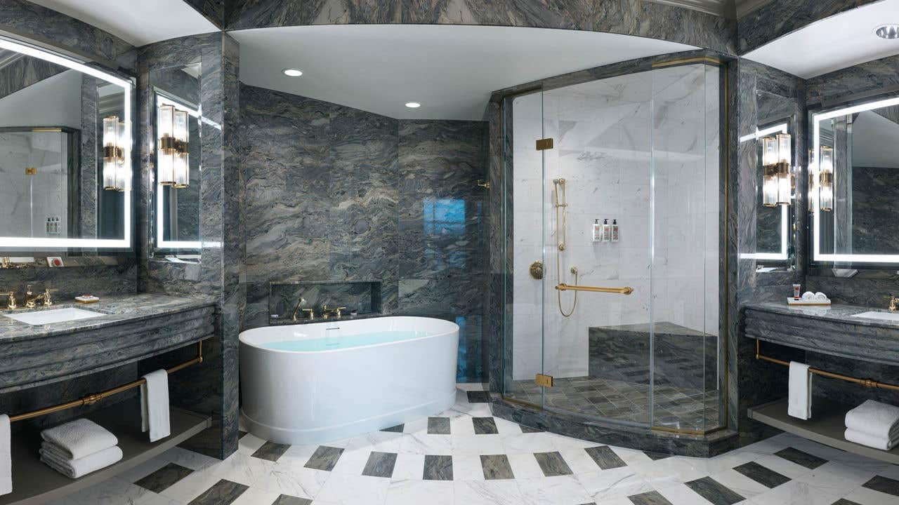 A hotel bathroom with a Roman bathtub, glass-door shower, and two separate sink vanities.