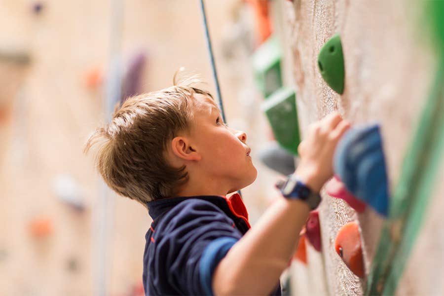 Young boy climbing an indoor rock wall, gripping colorful holds, and wearing a blue shirt.
