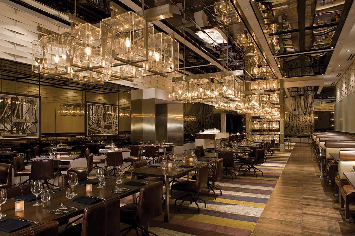 Luxurious modern restaurant with elegant chandeliers, wooden tables, leather chairs, and contemporary wall art.