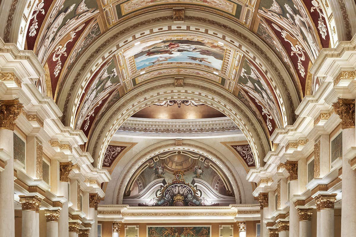 Ornate ceiling with intricate murals, arches, and columns in a grand hall, showcasing classical architecture and opulent details.
